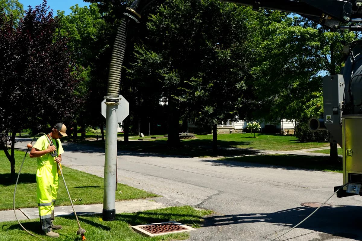 A crew member running the vacuum hose on a residential street, the boom overhead.