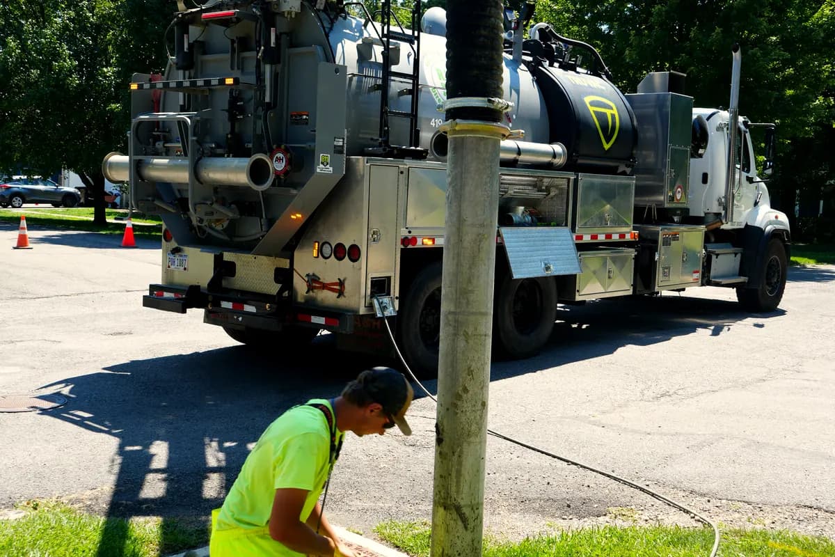 A crew member potholing at the base of a utility pole while the vac truck holds suction on the hole.