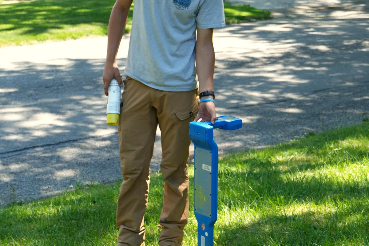 A crew member walking a utility locator across a lawn before any digging starts.