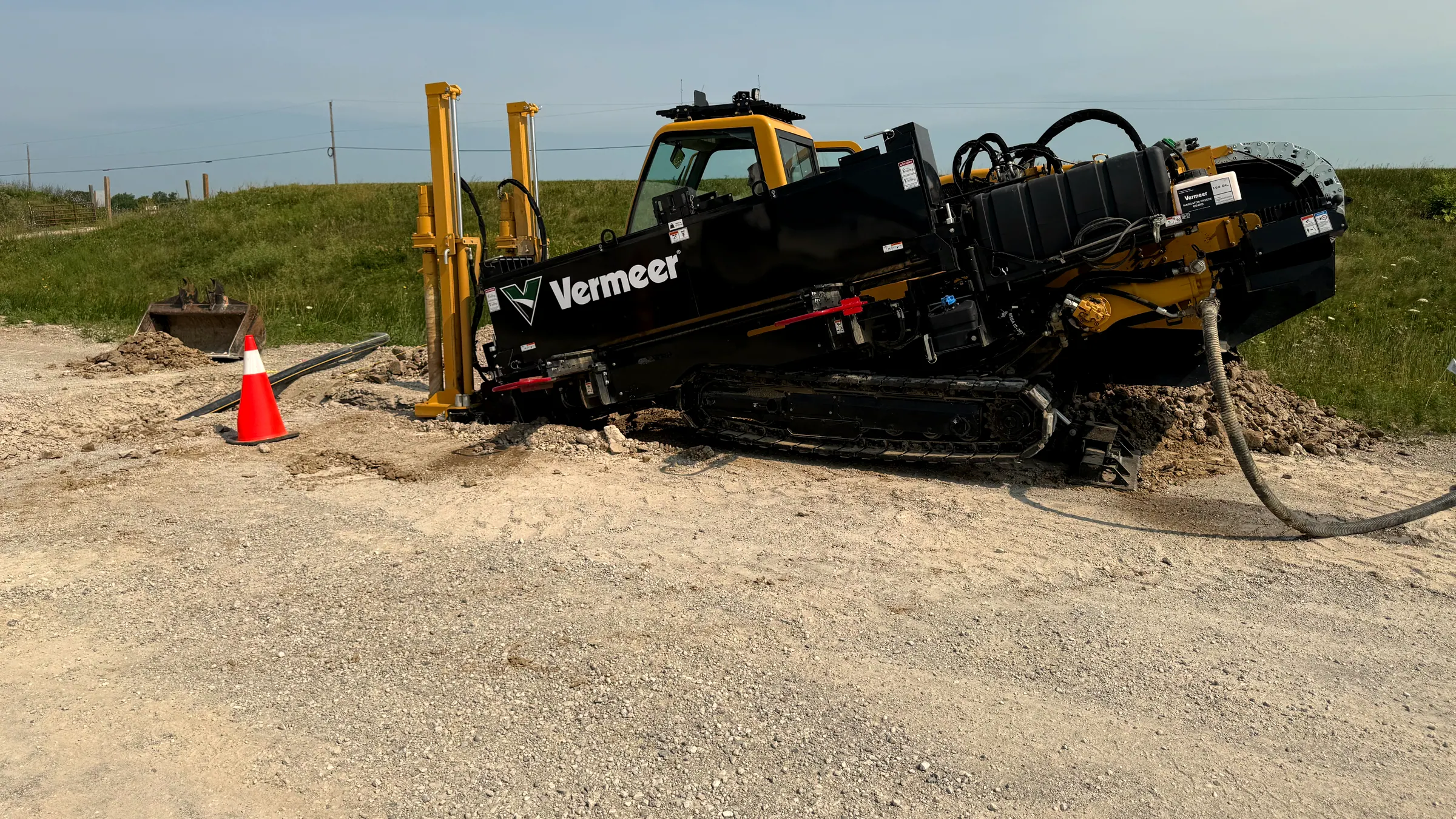 The Vermeer D24x40 set up at the edge of a road, anchored and boring, with spoil piled behind the tracks.