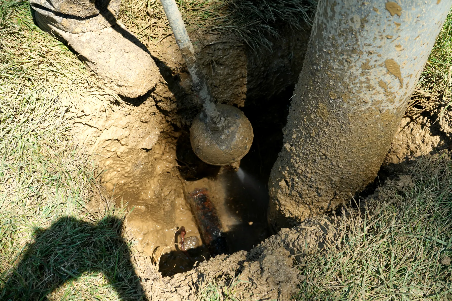 A buried line exposed intact at the bottom of a hydro-excavated hole, the water wand still working the soil away from it.